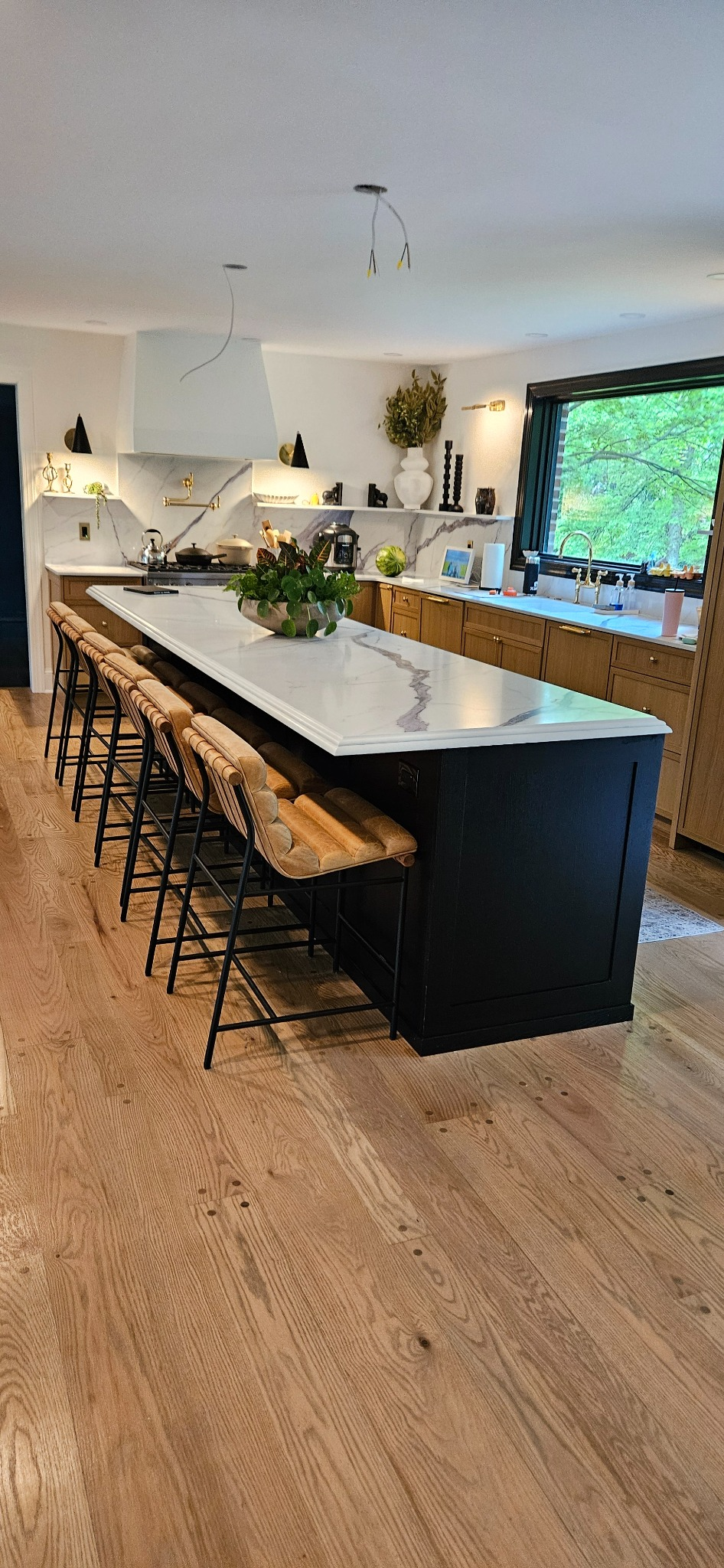 White oak custom kitchen cabinetry with a long black painted island, marble countertops and a custom hood surround
