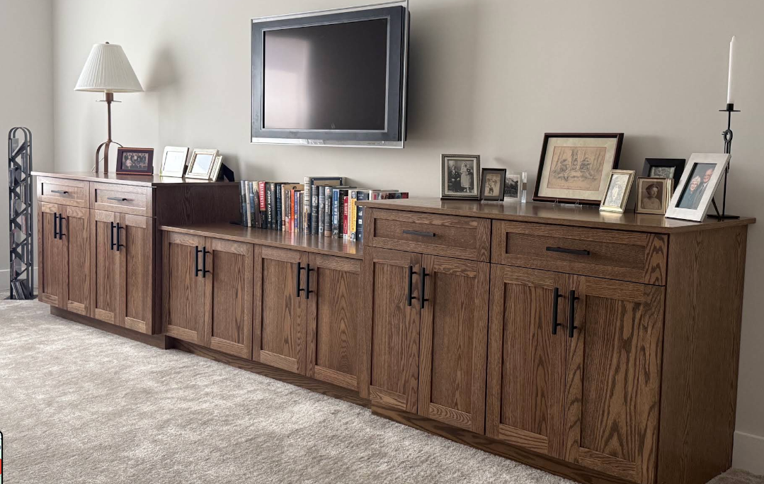 Stained oak custom media built-in cabinetry with drawers, closed storage and an open book shelf bay