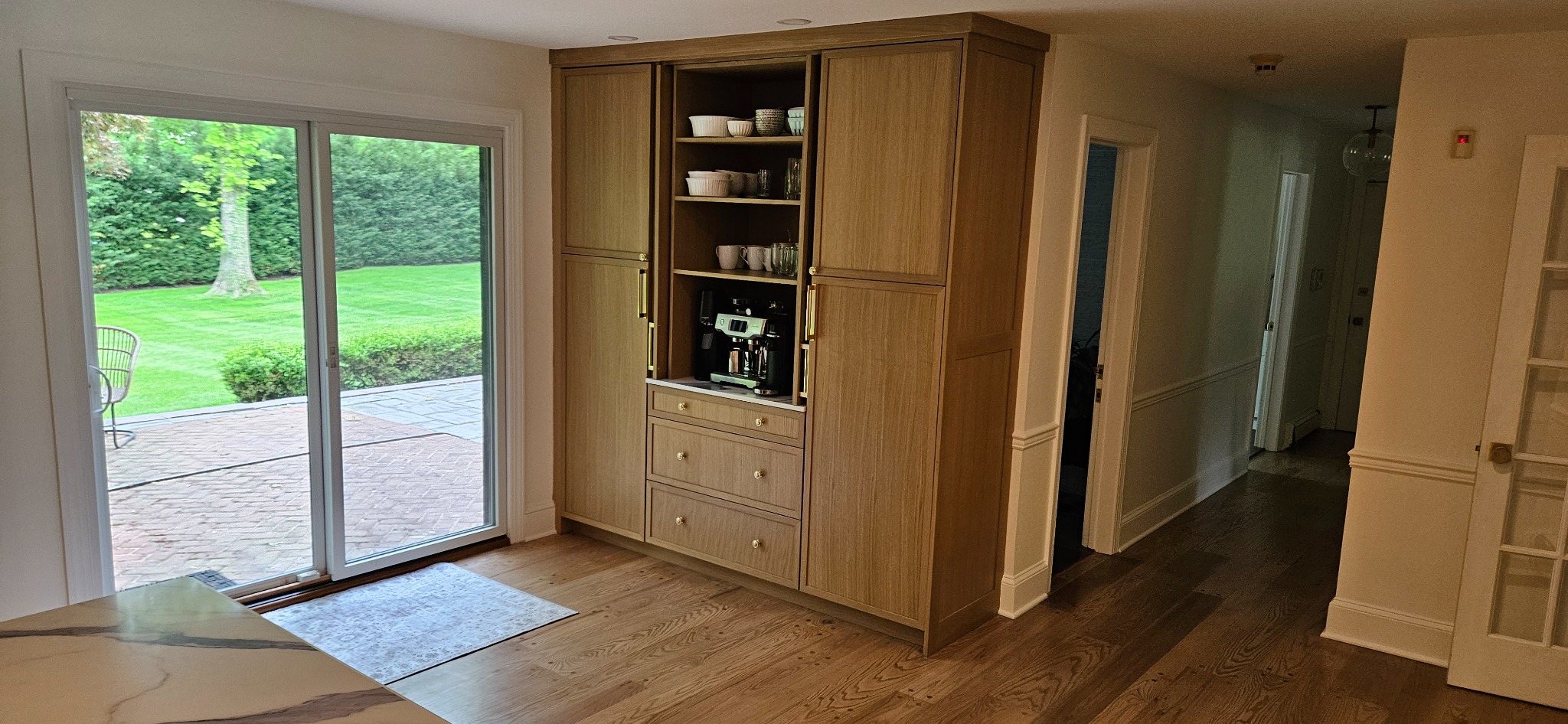 White oak custom coffee and beverage bar with tall pantry cabinets, open shelving, an appliance bay and brass hardware