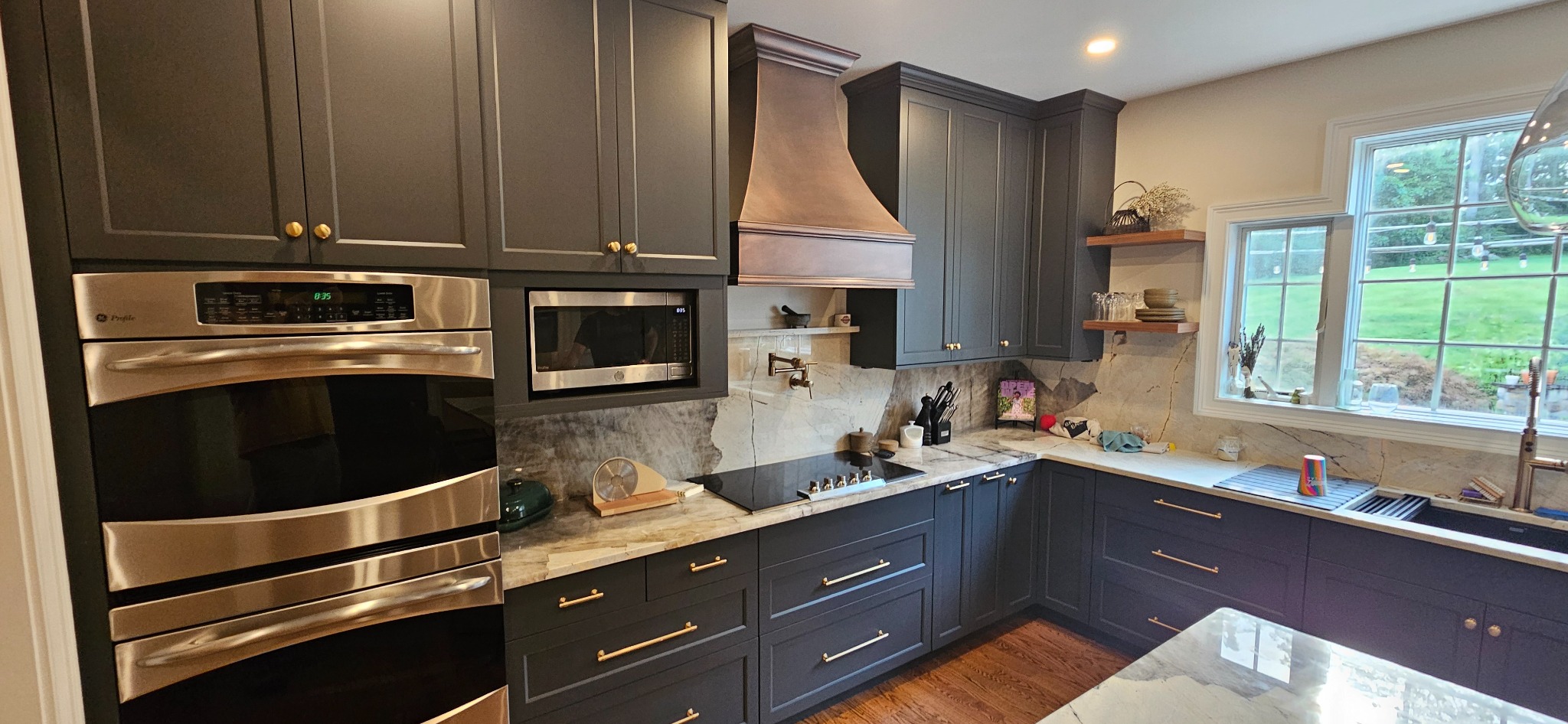 Detail of the dark painted kitchen showing the copper hood, wall ovens, stone backsplash and brass hardware